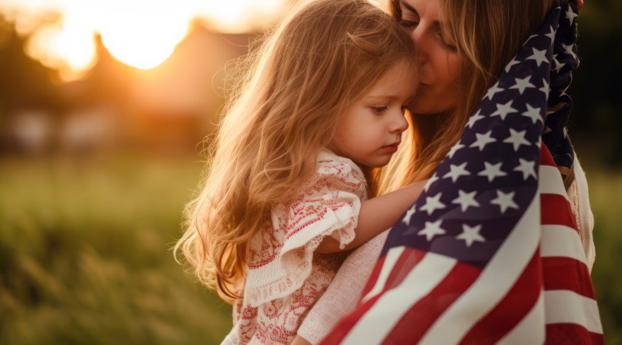 Mother hugging child with US flag at sunset