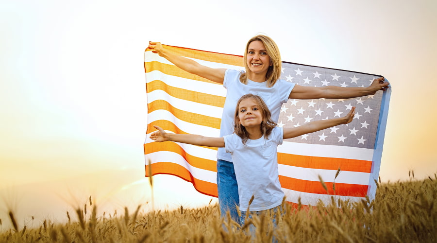 Mother and child holding striped US flag in field.