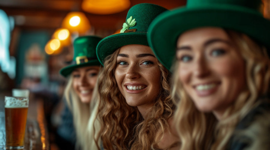 3 smiling women wearing green hats with clover decorations, celebrating St. Patrick's Day