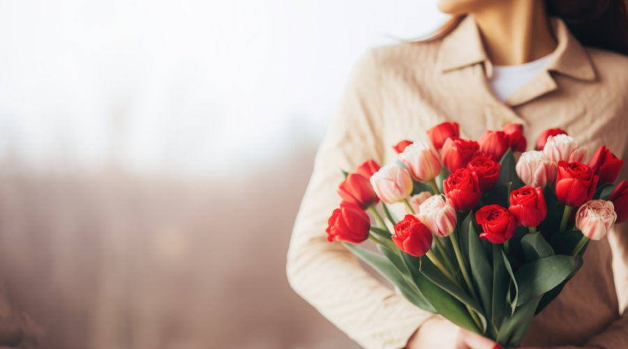 Person in a beige coat holding a bouquet of red and white tulips