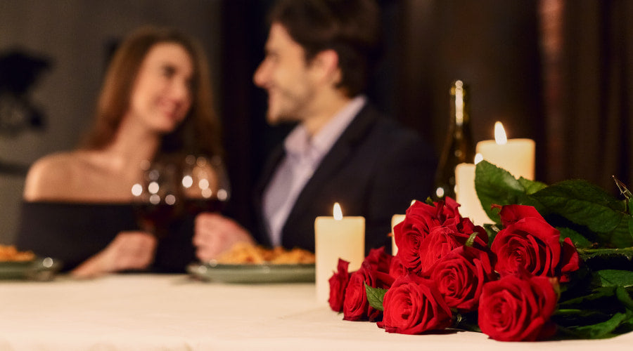 Couple toasting with wine behind a bouquet of red roses on a table