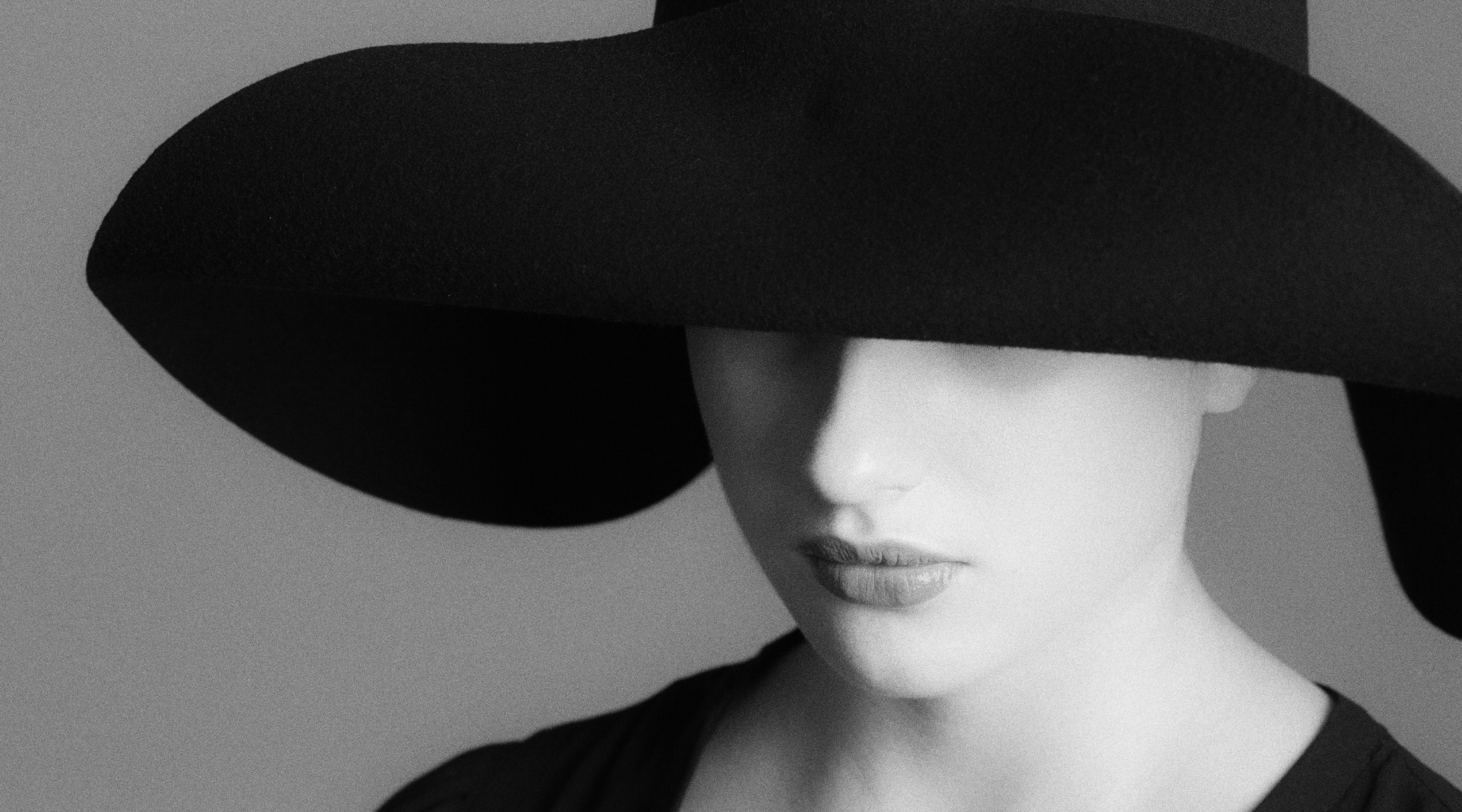 Schwarz-Weiß Foto einer Person, die einen schwarzen Hut trägt, der ihr Gesicht zu großen Teilen bedeckt.