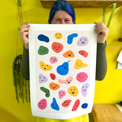 Emoji Mood Emotions Poster, different emoji feelings on brightly coloured blobs, the paper poster being held up in a yellow room