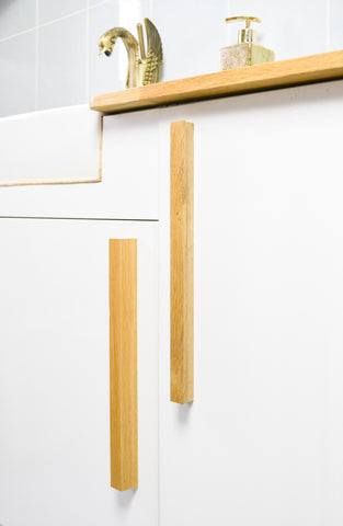 Oak drawer pulls in a bathroom setting, white cabinets and sink with a gold swan tap