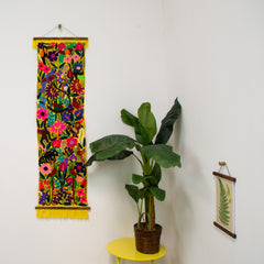 Magnetic hanger holding a woollen rug on the wall, next to a plant on yellow table and magnetic print hanger holding a print
