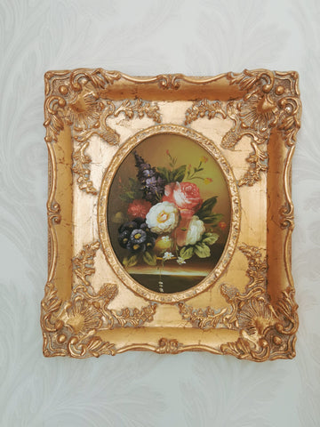 small painting of flowers in a large, ornate gilt picture frame