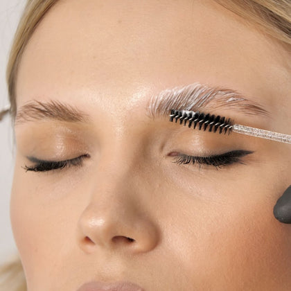 A girl getting a solution spread over her brows with a brow brush