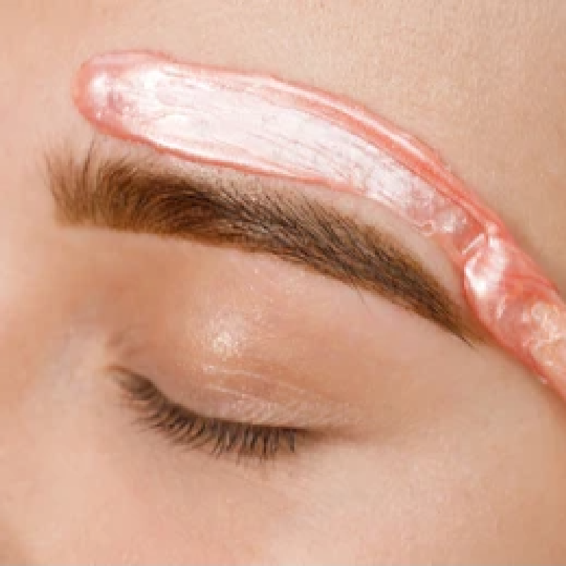 Pink wax being spread above a person's eyebrow