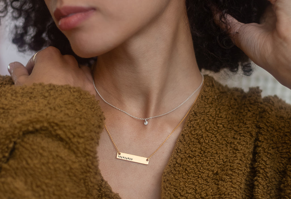 model with gold medium ID necklace with TREASURED stamped and a small silver seedling pendant with diamond dusted finish