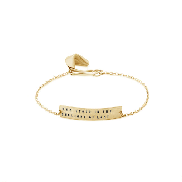 gold fortune cookie bracelet with message reading "she stood in the sunlight at last"