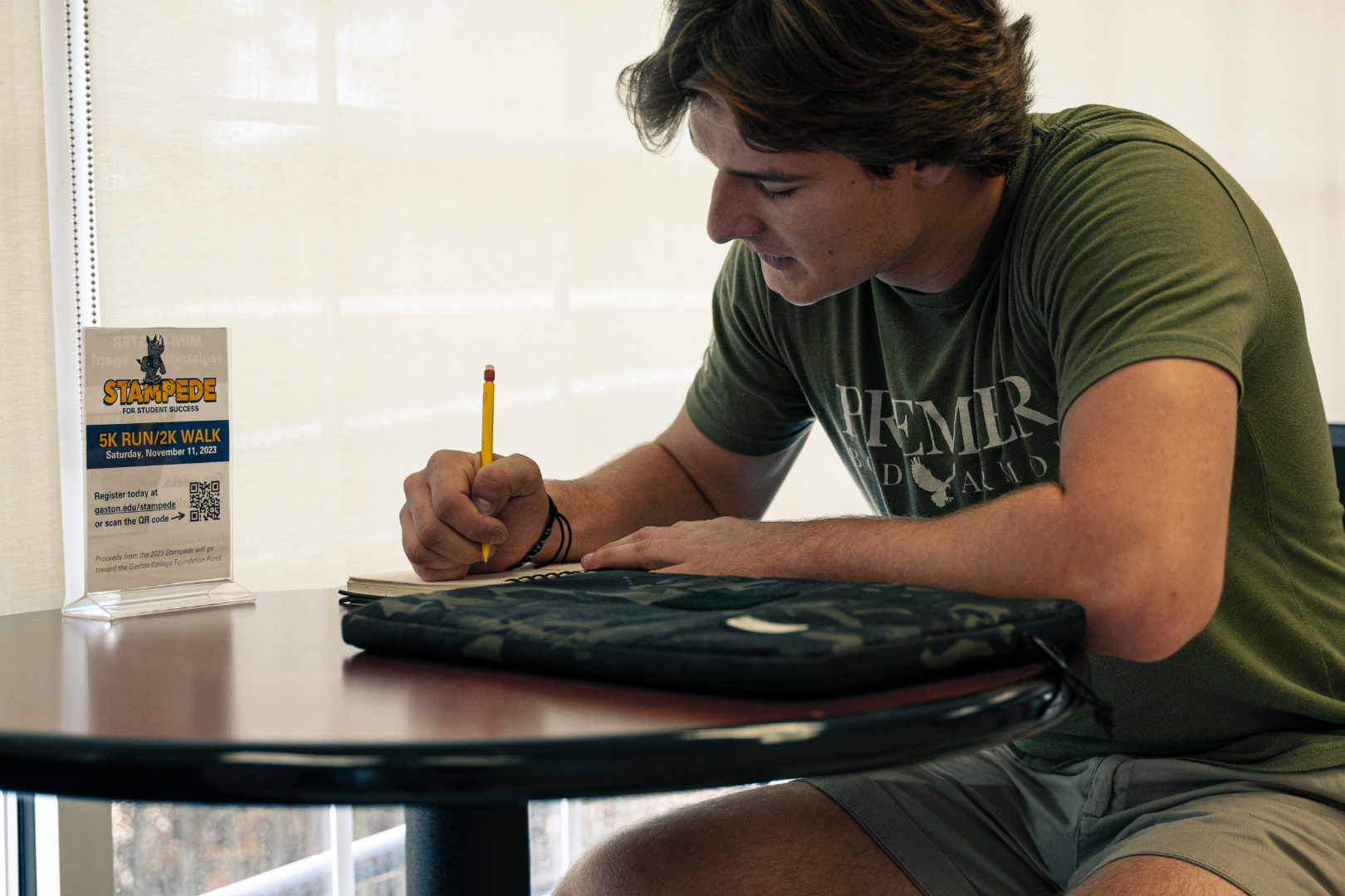 student in library writing in notebook with laptop case on table