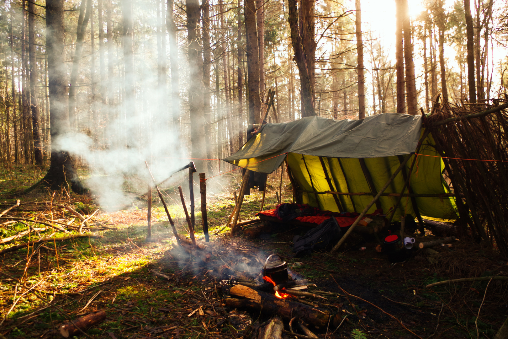 bushcraft campsite with tarp tent and fire