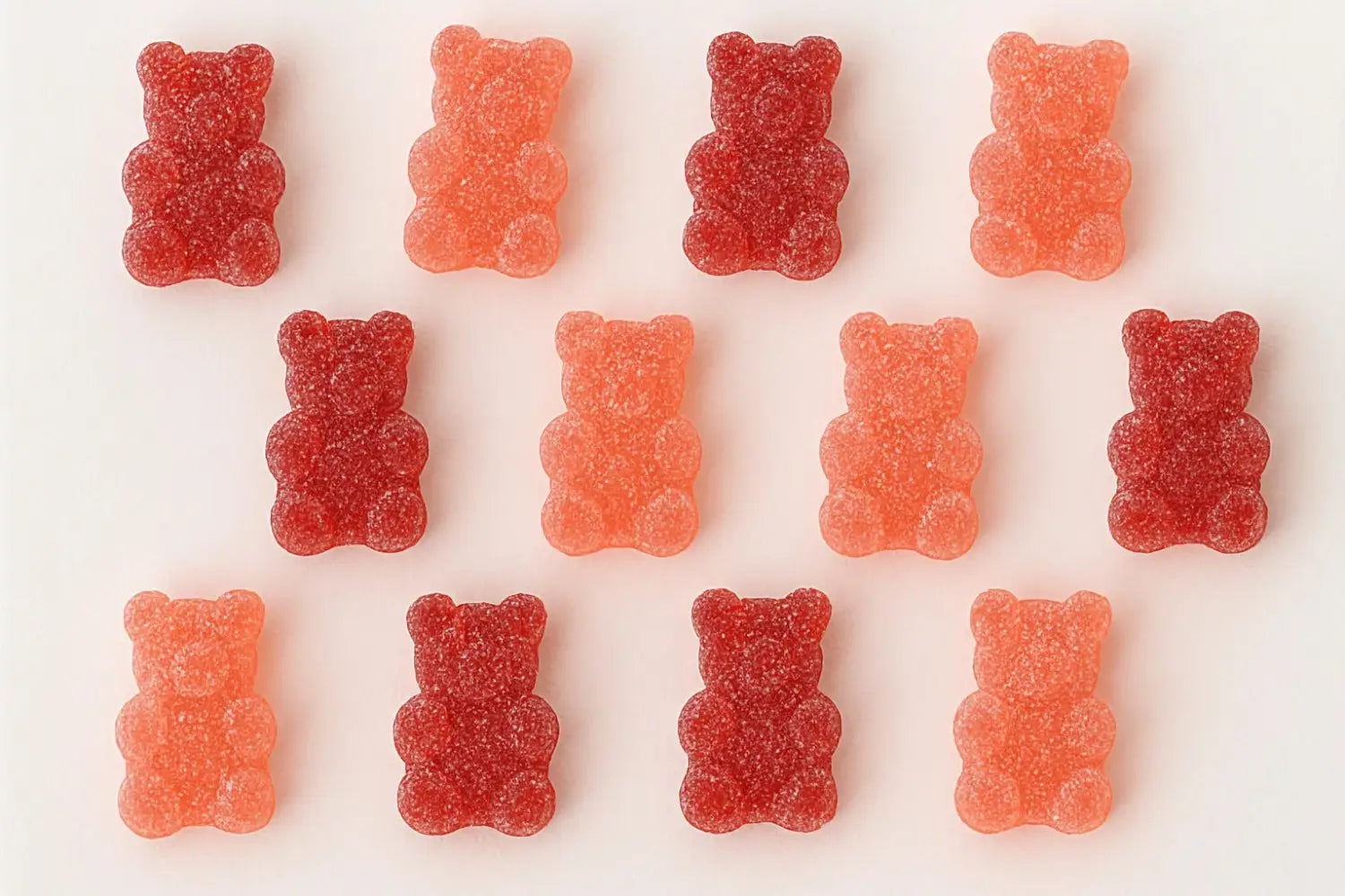 Red and orange gummy bears neatly arranged on a white background with a sugar coating.