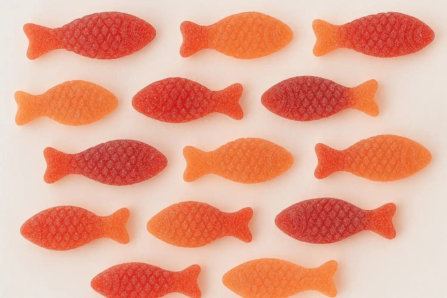 Orange and red gummy fish candies laid out in rows on a white background, covered in sugar granules.