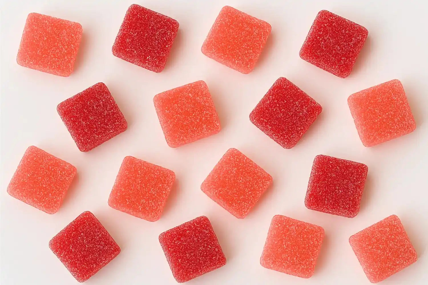 Red and orange square-shaped gummy candies on a white background, dusted with sugar crystals.