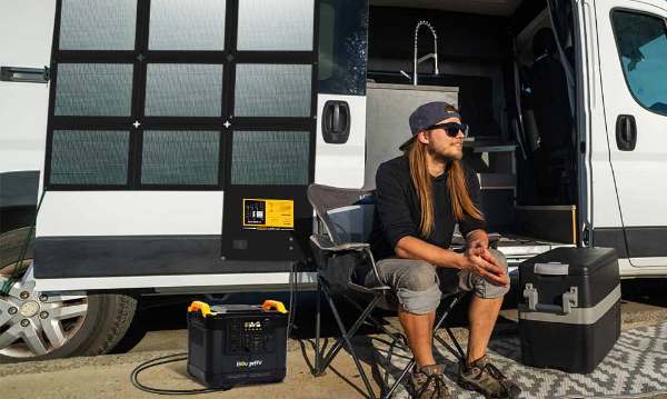 A man sitting with a folding solar panel on the RV behind him