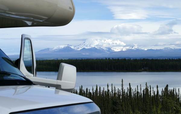 An RV is parked near a serene lake, offering a stunning view of the surrounding nature