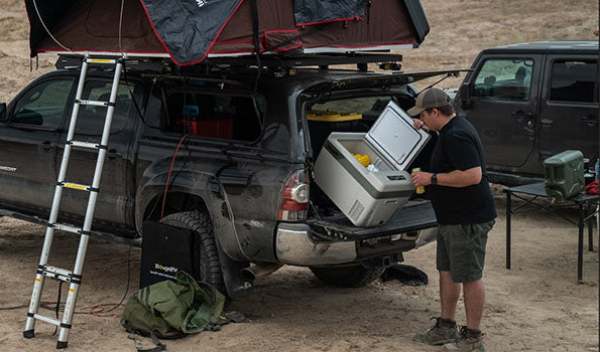 A man takes food out of a BougeRV 12V portable mini fridge during an overloaded camping trip