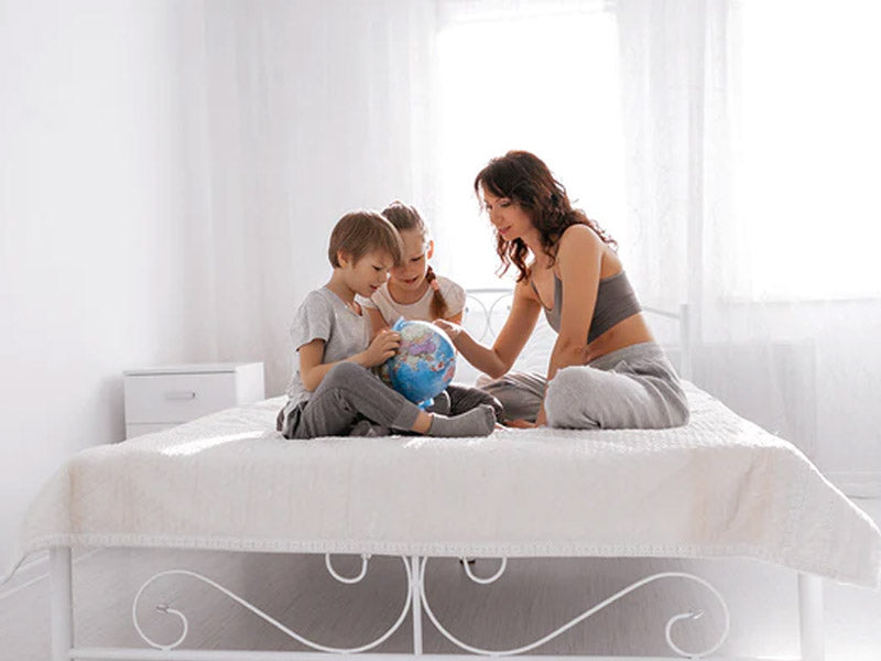 mother guiding children using a globe on bed