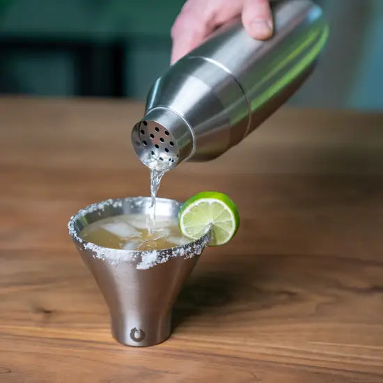 Pouring a cocktail from a stainless steel shaker into a glass