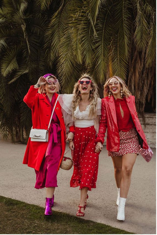 Three women in pink and red shades hold hands and walk outside