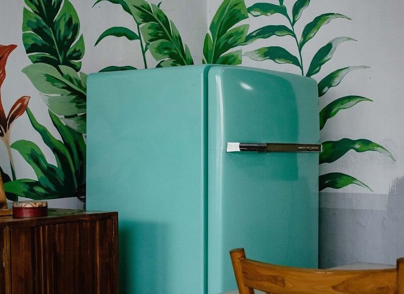 Turquoise refrigerator in the corner with floral wallpaper behind it