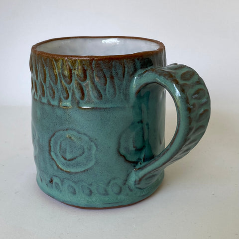 Slab built mug with a textural design of circular rings and tear drops created with a handmade stamps and roulettes in an exterior turquoise glaze and white liner glaze