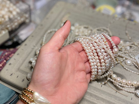 Handmade Jewellery in the making a the RAW Studio, image shows a hand holding lots of freshwater pearls over a beading tray