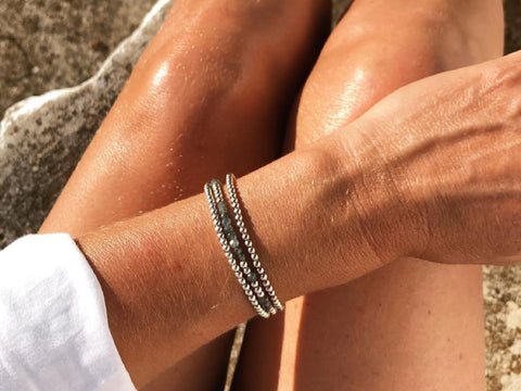 Eco-silver wrap bracelet modelled on tanned wrist resting on legs in the sun