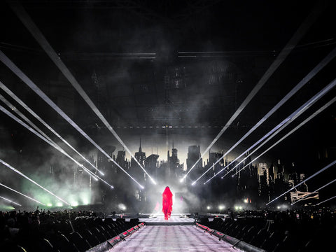 A figure cloaked in red walks across the stage