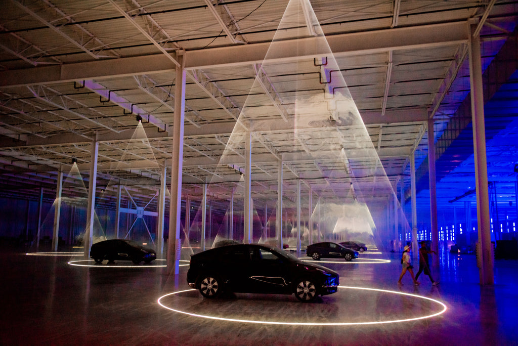 Spectrum lasers mounted from ceiling, projecting bright laser circles around Tesla vehicles at Tesla Gigafactory