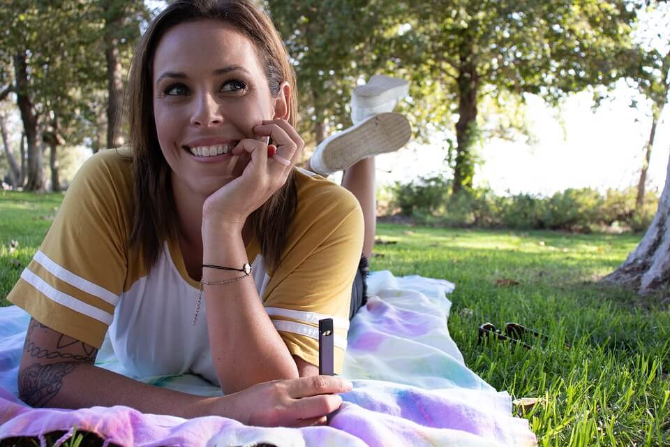 woman lying in park holding vaporizer