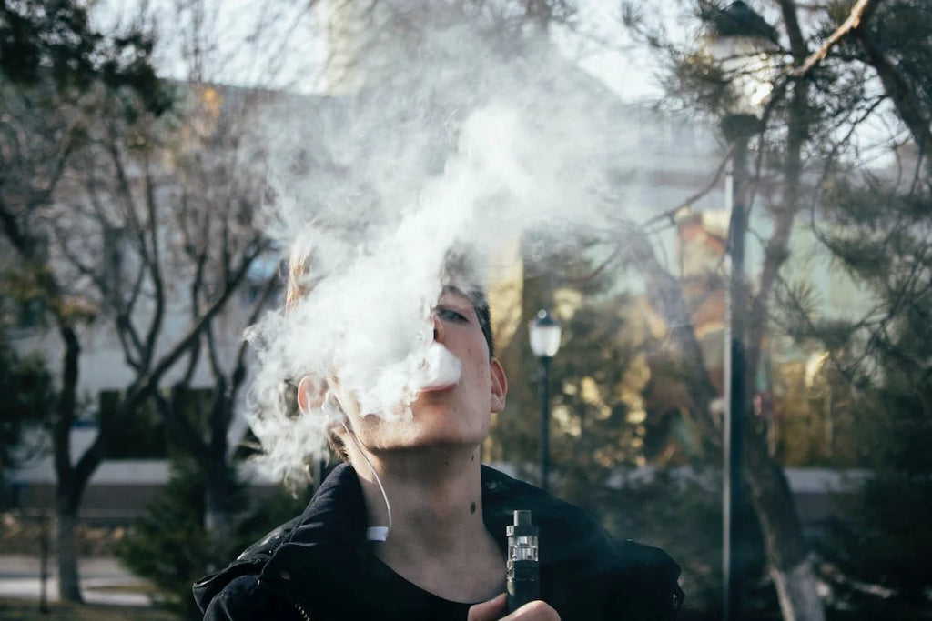 young man blowing smoke from a vape into the air