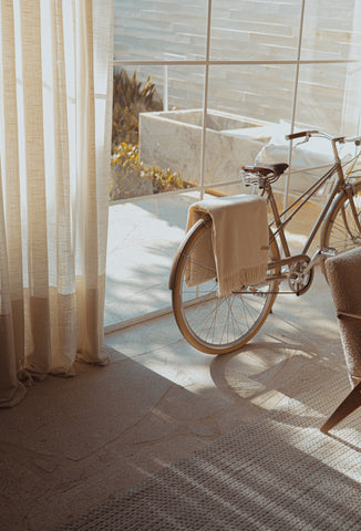 Home interior featuring a close up of a full height window glass view to the patio. A bicycle is parked inside the room and has a beige throw folder over the rear tire. Home interior and exterior features a soft and soothing beige color palette.