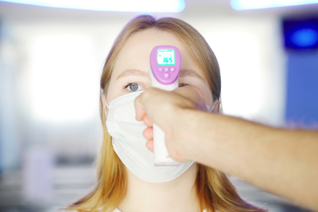 A person easily uses a contactless thermometer to test for covid-19 without the risk of cross contamination, by simply pointing the thermometer at their forehead and pressing the start button