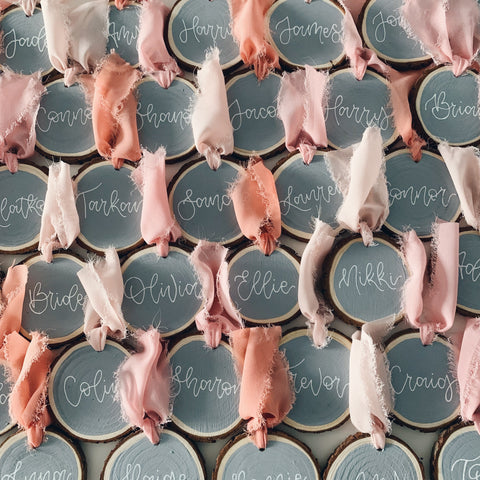 wedding place cards on a grey wooden slice with dyed silk cotton in pastel pinks