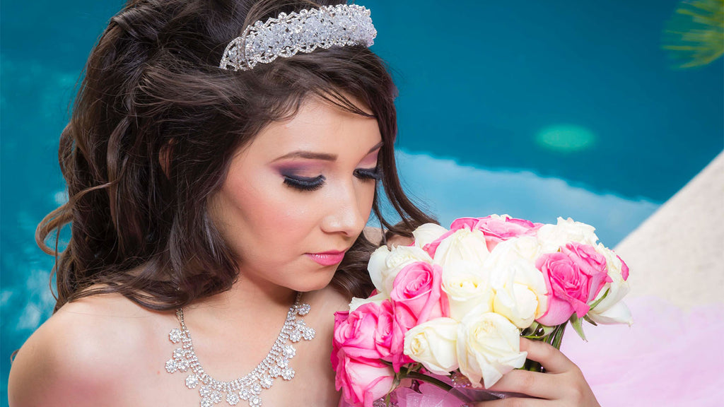 girl dressed up for her quinceanera with a tiara crown on her head smelling the flowers