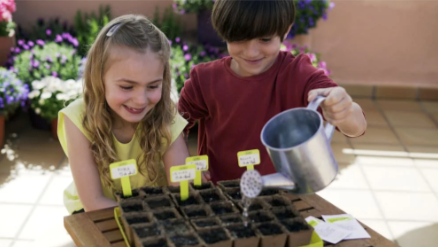 Blonde girl and brunette boy smiling and watering their seeds on the patio