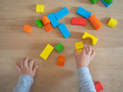 Child's hands playing with colourful wooden shapes on a wooden surface