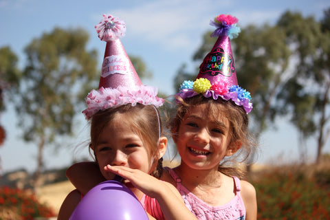 two girls in pink party hats smiling and holding a purple balloon