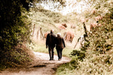 Two elderly people walking through a wood side by side in order to support the lady with dementia  