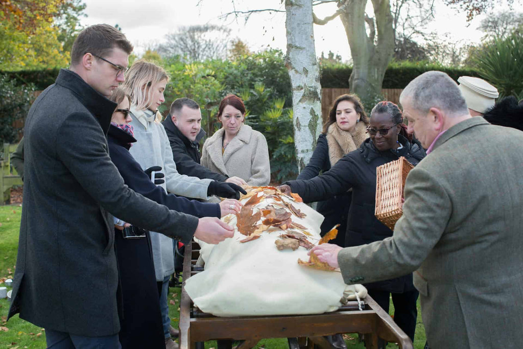 People honouring the memory of the deceased by laying leaves on the pall