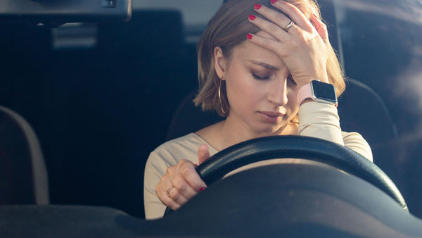 Woman in car that is looking down in pain holding head from migraine pain 