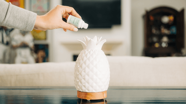 Hand pouring MOXĒ Eucalyptus Essential Oil into pineapple-shaped diffuser 