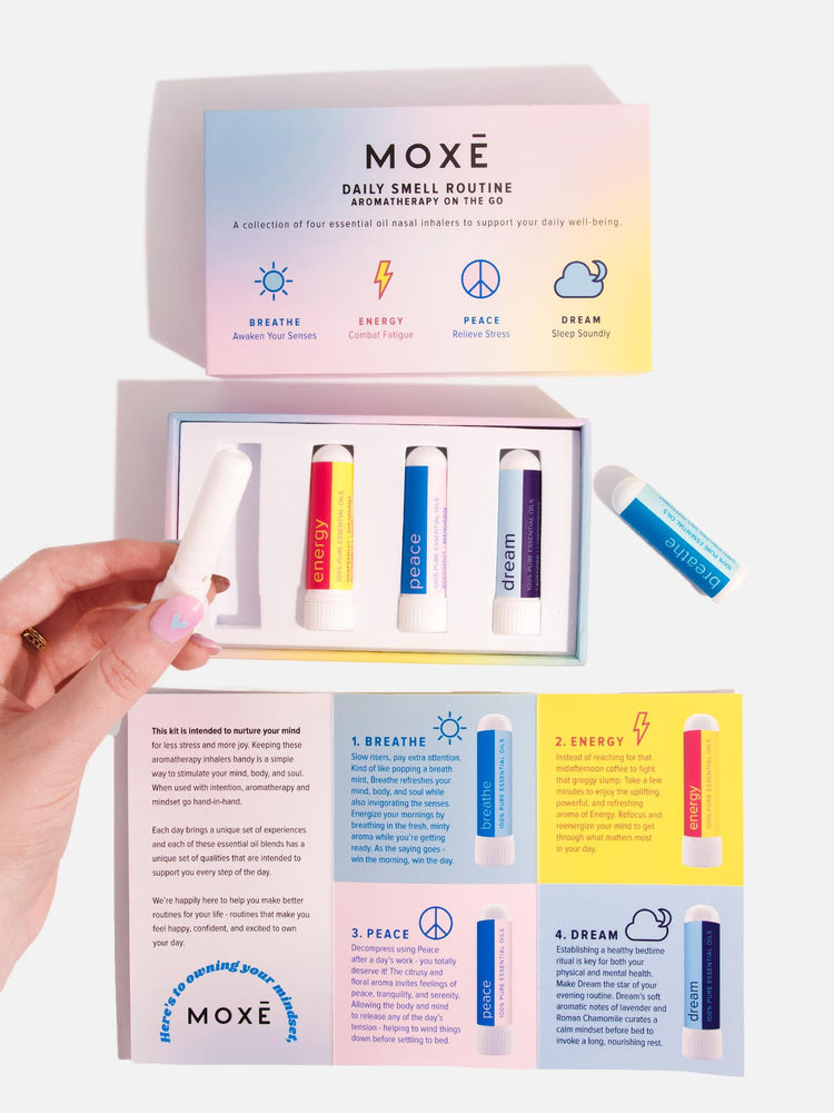 Girl's hand holding MOXĒ Breathe Aromatherapy Nasal Inhaler above a opened MOXĒ Daily Smell Routine - Inhaler Kit