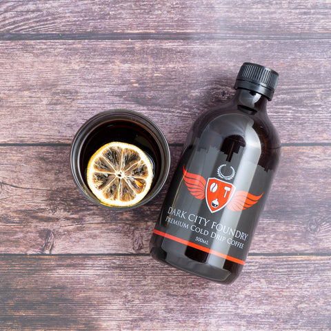 cold drip coffee in a glass with dehydrated slice of lemon. Next to a bottle of 500ml cold drip coffee. image is a flatlay