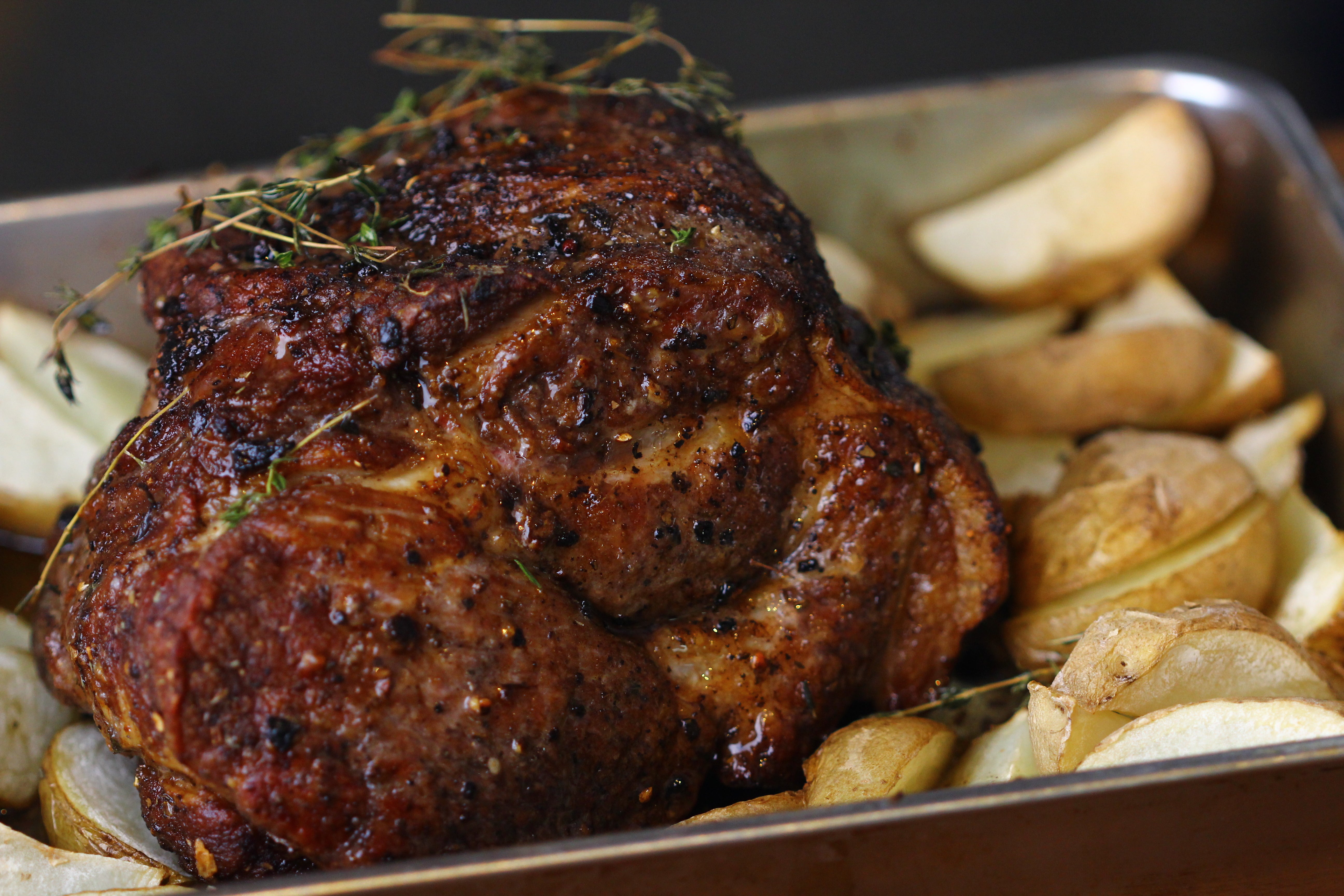 Roasted pork shoulder with its bed of potatoes and thyme