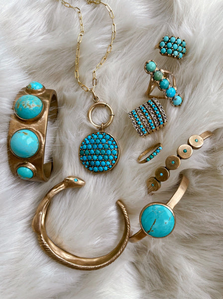 An assortment of Madeline's turquoise jewelry is laid out on a white faux fur background