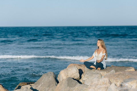 woman meditating on rock by ocean