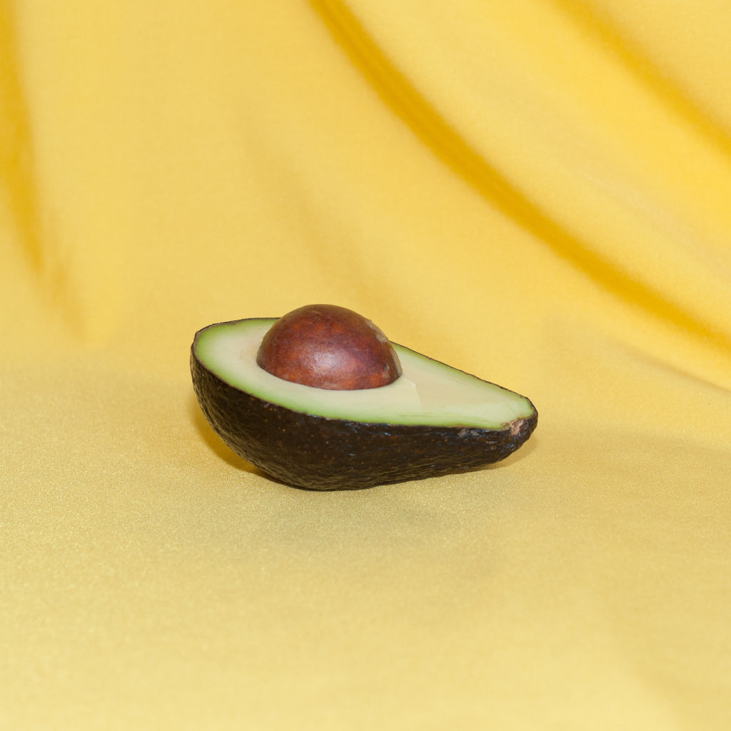half an avocado with pit on a yellow fabric background